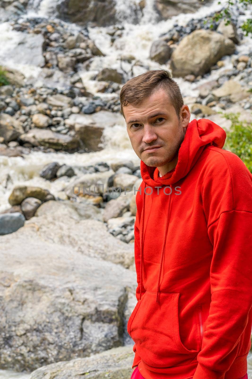 Portrait of young man looking away on background of waterfall. Adult male tourist enjoying beautiful view in mountainous area. by epidemiks