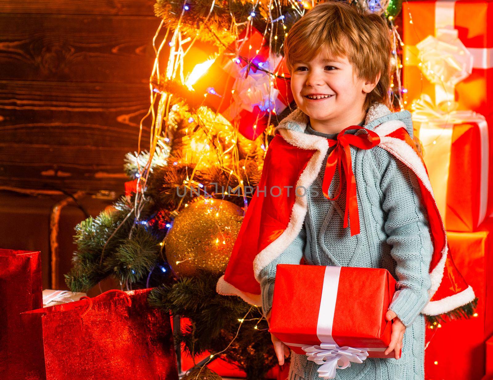 Happy smiling boy holding his Christmas present. Surprised kid at New Year decorated background. Family winter holidays and people concept. Childhood moments. Christmas attributes