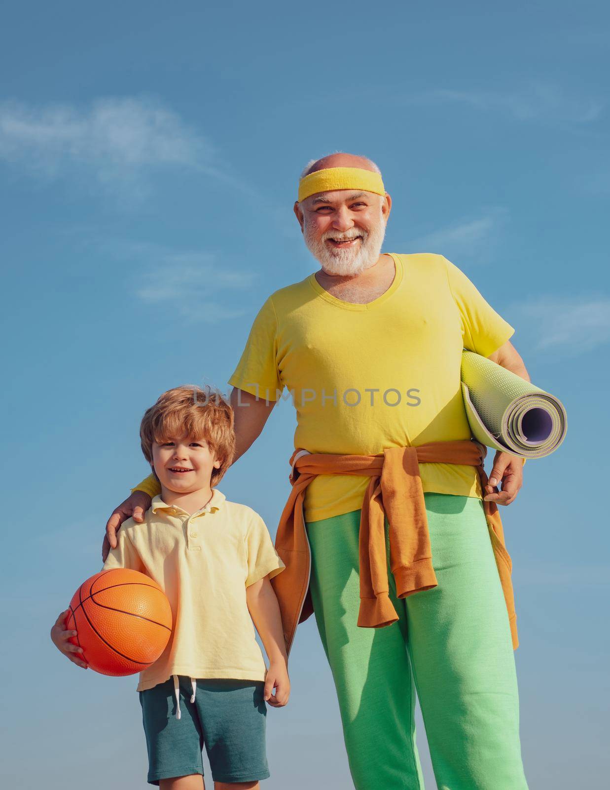 Rehabilitation. Grandfather and son doing exercises. Senior man and cute little boy exercising on blue sky background - isolated. by Tverdokhlib