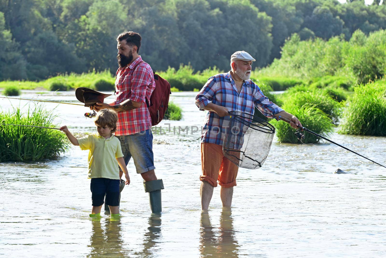 Men day. Family bonding. Fly fisherman using fly fishing rod in river. Fly fishing for trout. Grandfather and grandchild. Great-grandfather and great-grandson. by Tverdokhlib