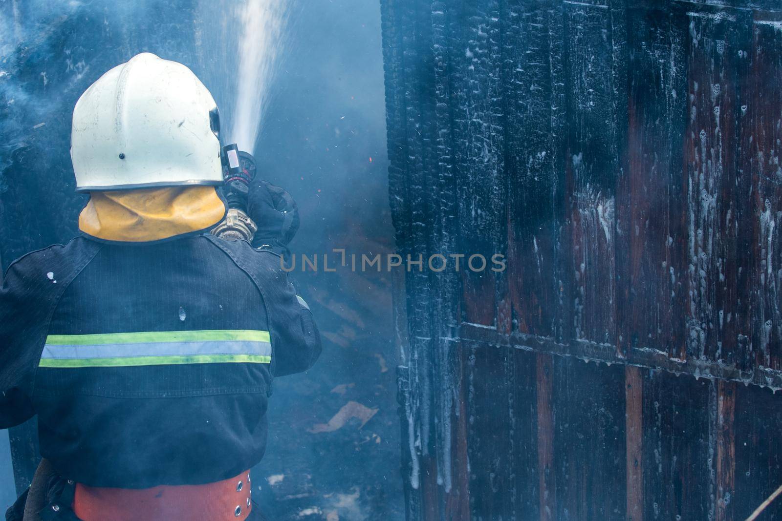 Fireman - men job. Firefighter spraying high pressure water to fire. Firefighter training with dangerous flames. Strong brave firefighter using extinguisher and water from hose for fire fighting