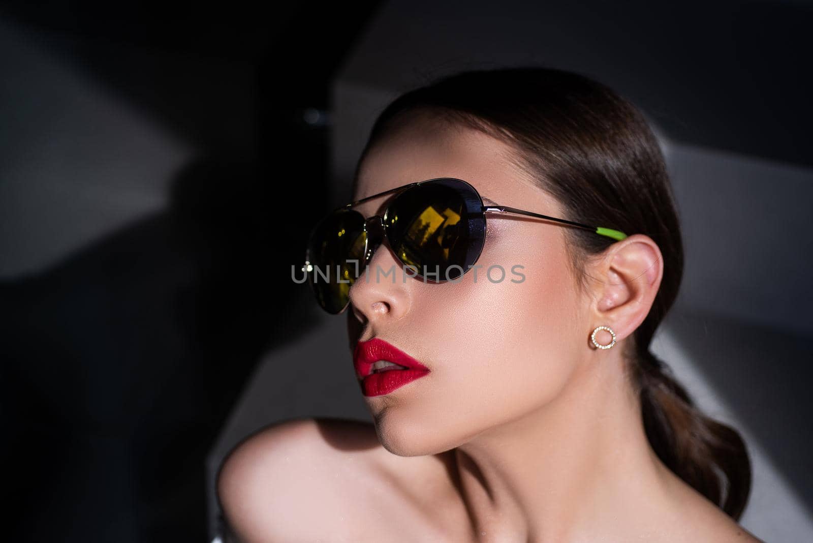 Elegant chic female model in fashion sunglasses with red lips. Portrait of serious woman in the dark isolated. Young woman posing. Portrait of a young woman in sunglasses