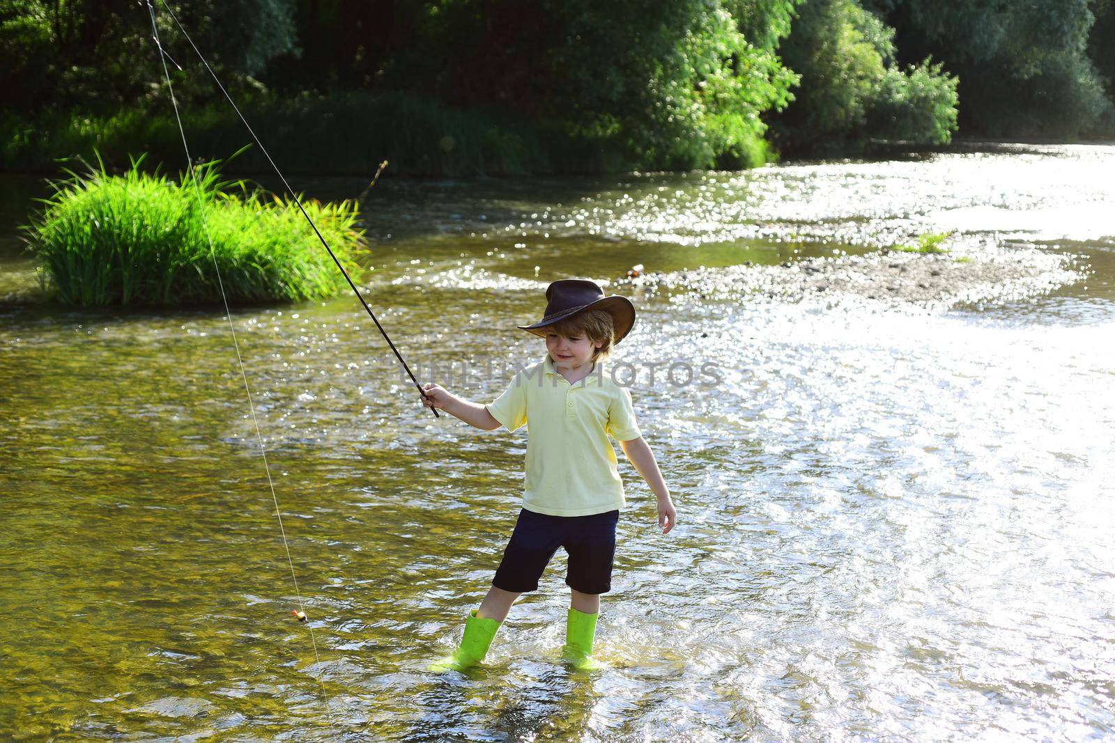 Child fishing. Kid learning how to fish holding a rod on a river. Little boy fisherman with fishing rod. Young man fly fishing