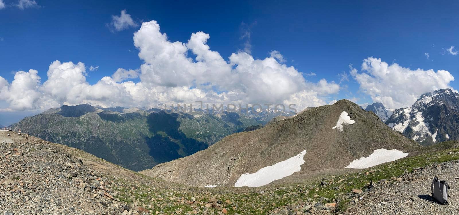 Panorama. Snowy mountain against cloudy sky. From below white clouds floating on blue sky over mountain ridge covered with snow on sunny day in nature by epidemiks