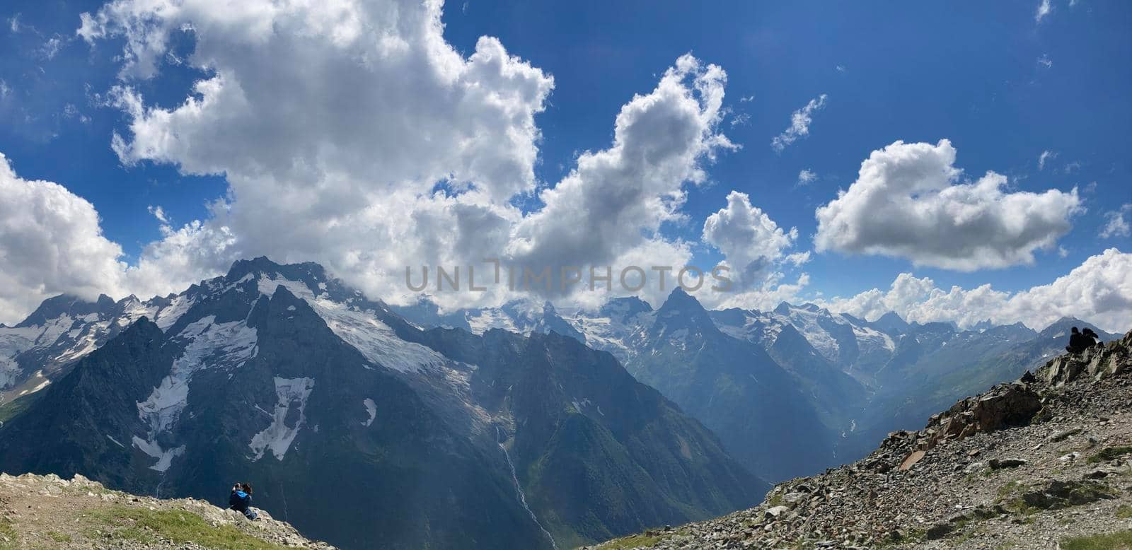Snowy mountain against cloudy sky. From below white clouds floating on blue sky over mountain ridge covered with snow on sunny day in nature by epidemiks