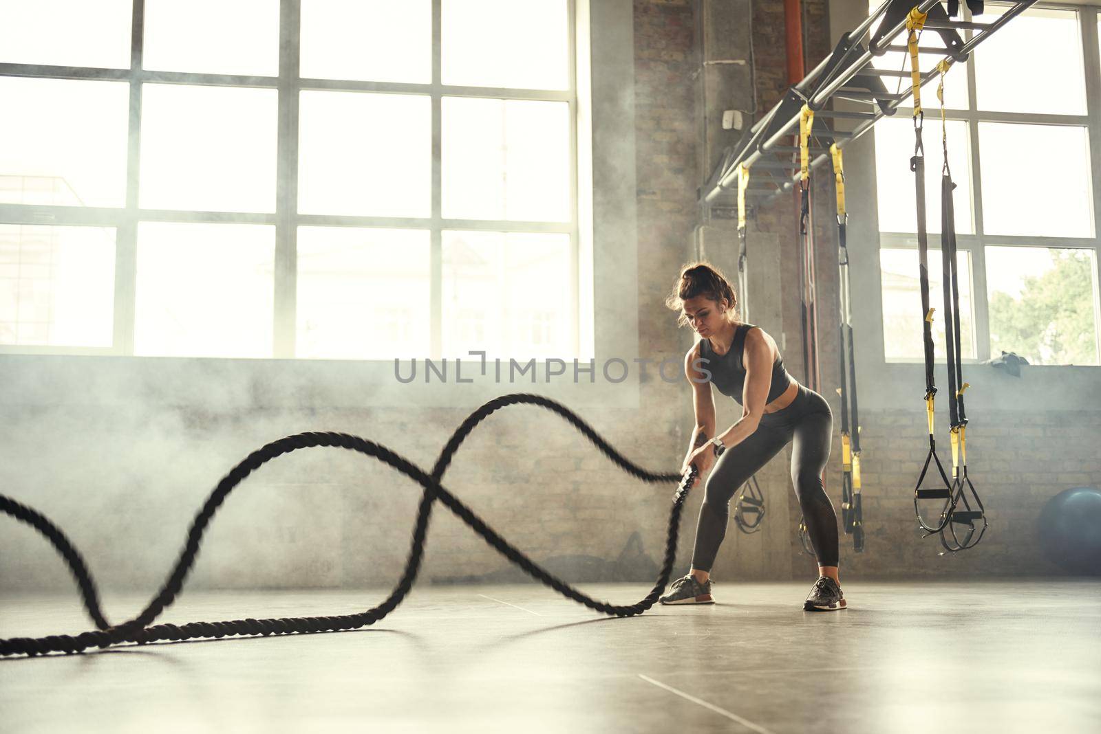 Strong and beautiful. Young athletic woman with perfect body doing crossfit exercises with a rope in the gym. by friendsstock