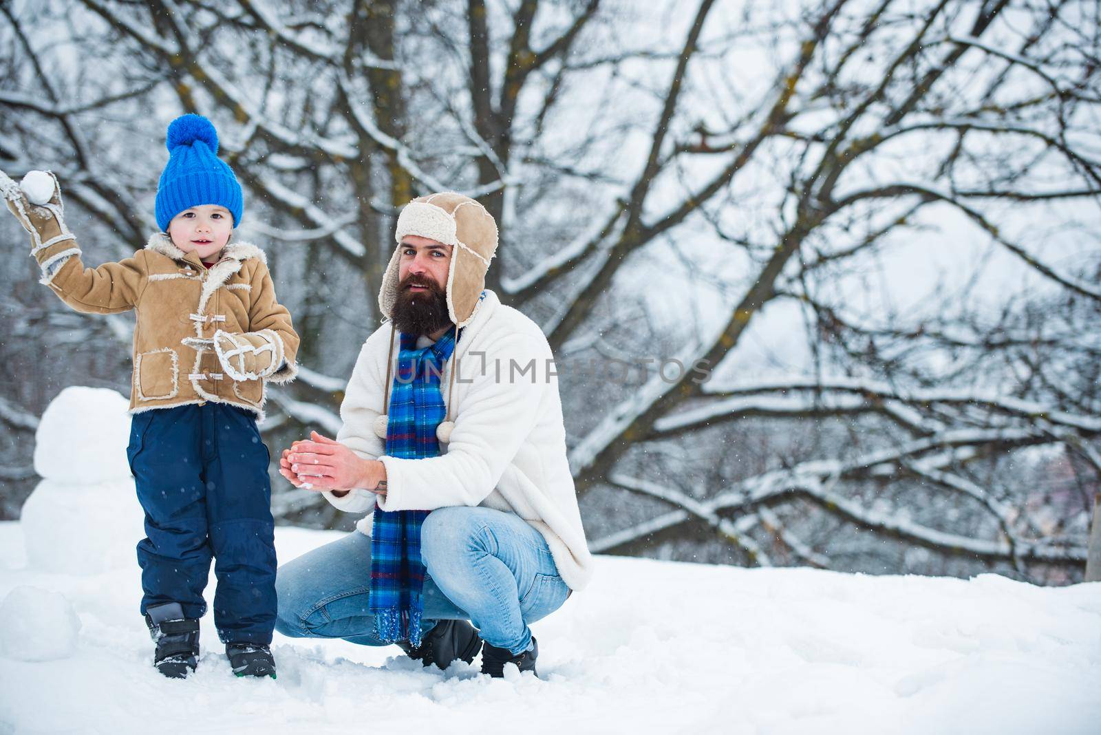 Happy father and son play on winter Christmas time. Fathers day. Happy child playing with snowball against white winter background. Happy loving family. by Tverdokhlib