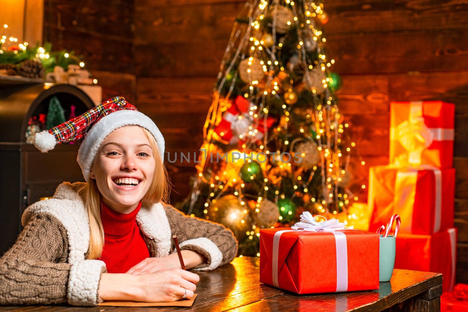 Cheerful smiling blonde woman writing a letter to Santa with her wish list of presents. Christmas presents gifts concept. Joy and happiness. Christmas. Xmas tree. by Tverdokhlib