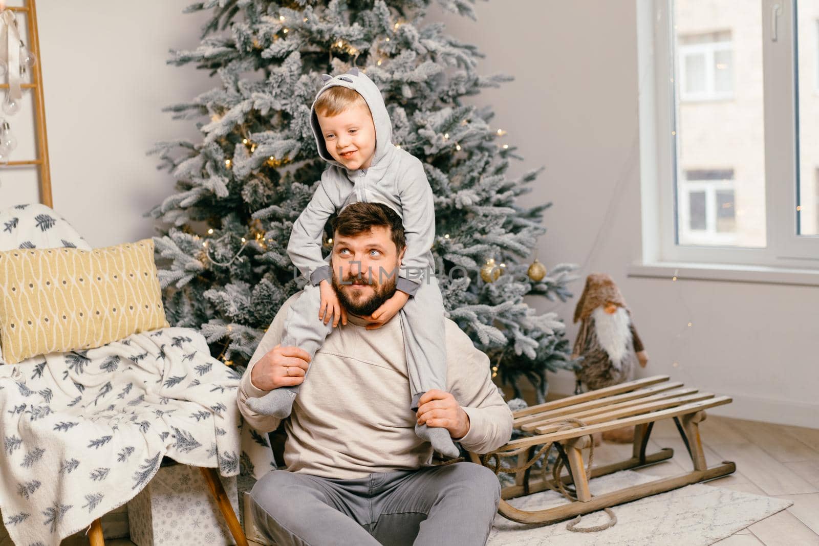 Holiday Christmas Handsome father playing with small cute son near decorated New year tree at home by andreonegin