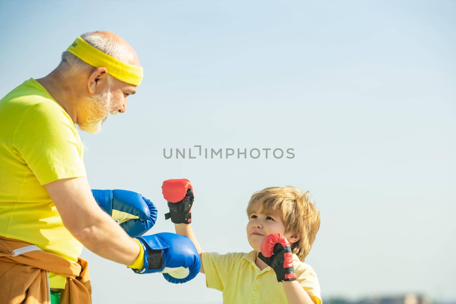 Handsome elderly man practicing boxing kicks. Elderly man hitting punching bag. Grandfather and child fighting poses. Senior trainer and little boy wearing boxing gloves