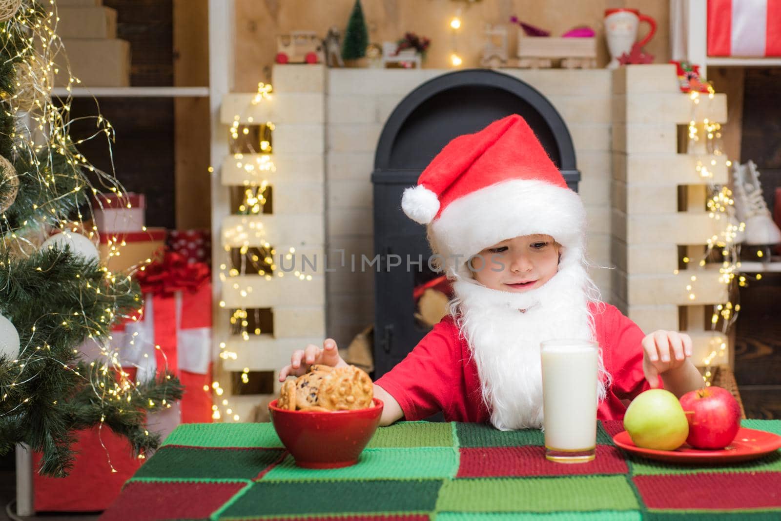 Little Santa picking cookie and glass of milk at home. Greeting Christmas card. Milk and gingerbread cookie for Santa against Christmas light background