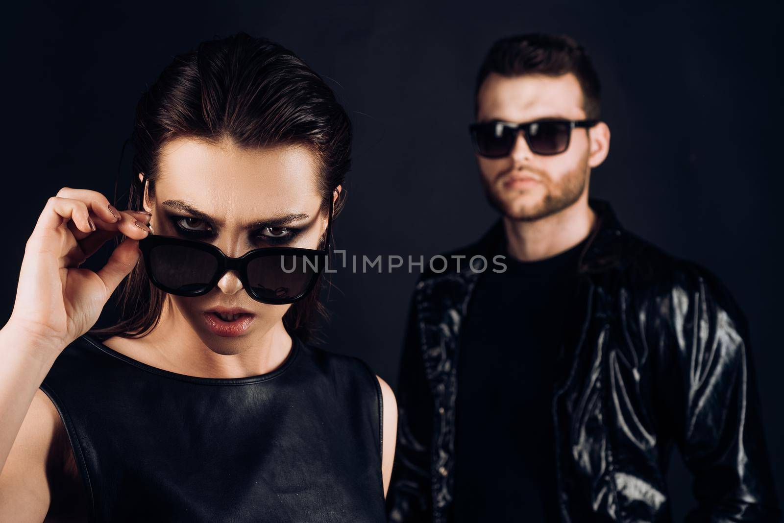 Boy in suits and a girl in an black glasses. Fashion photo of handsome man and woman. Man and woman on serious faces. Company of confident people friends. Isolated on black