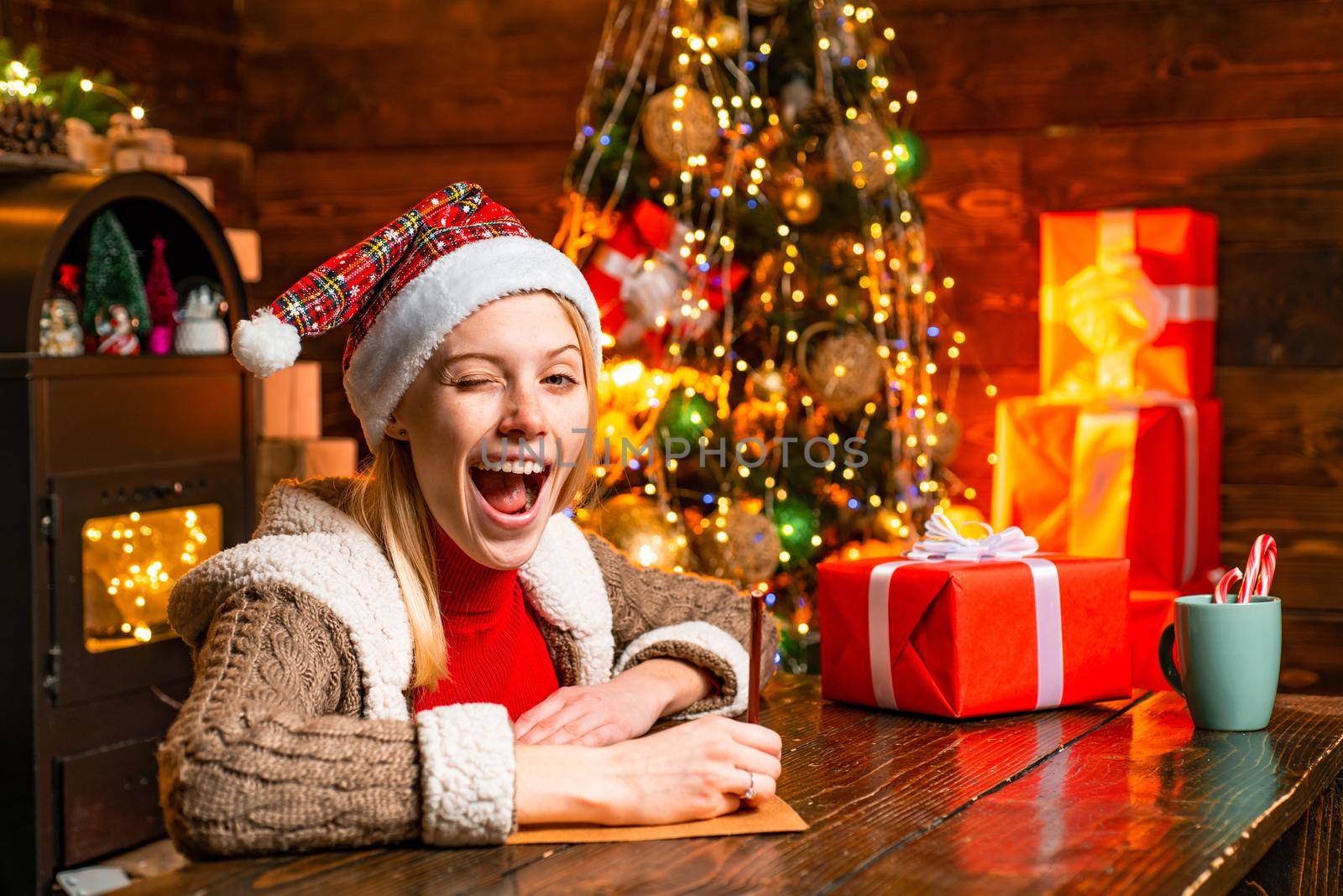 Eye winking blonde beautiful woman in Santa's hat at winter holiday background. Merry christmas and happy new year. It is miracle. Concept of winter holidays and good time