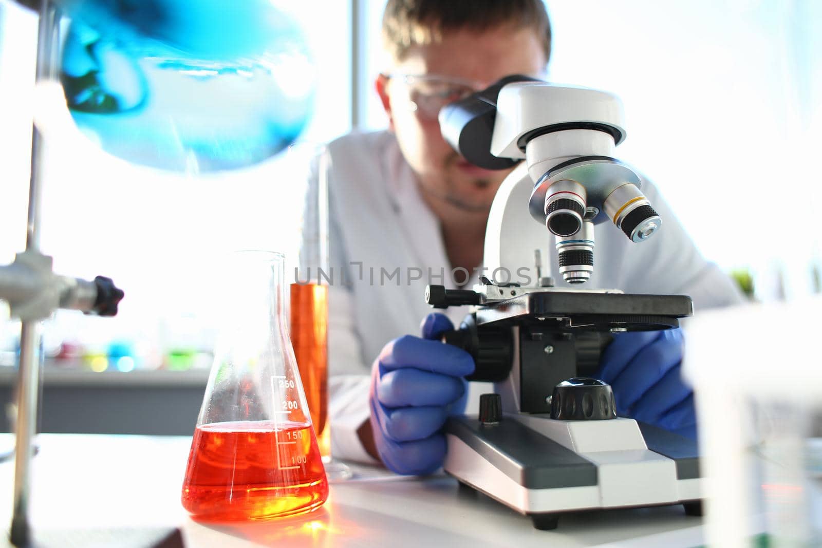 Portrait of a young chemist looking in binocular microscope looking for pathology analyzes patient at medical hospital for treatment disease tumors