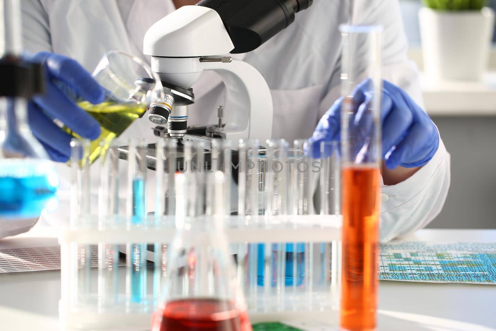 A male chemist holds test tube of glass in his hand overflows a liquid solution of potassium permanganate conducts an analysis reaction takes various versions of reagents using chemical manufacturing.