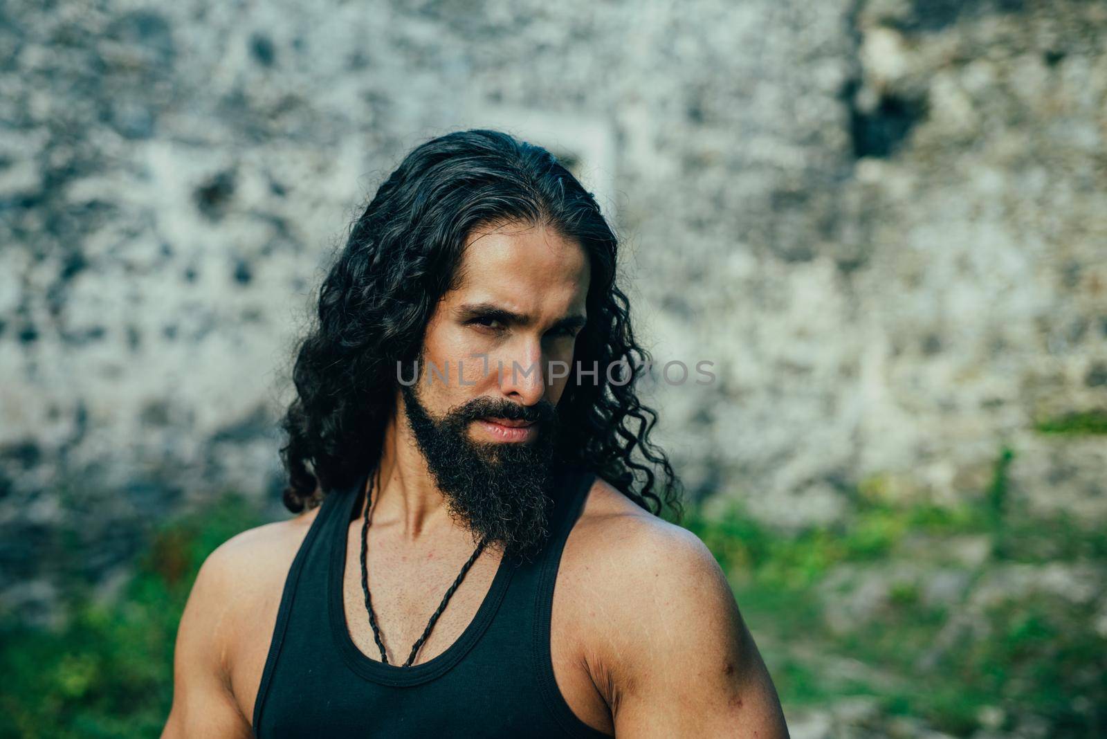 Young stylish man with determined character. Strong confident man with long wavy dark hair and beard looking at camera. Mans power and confidence concept. by Tverdokhlib