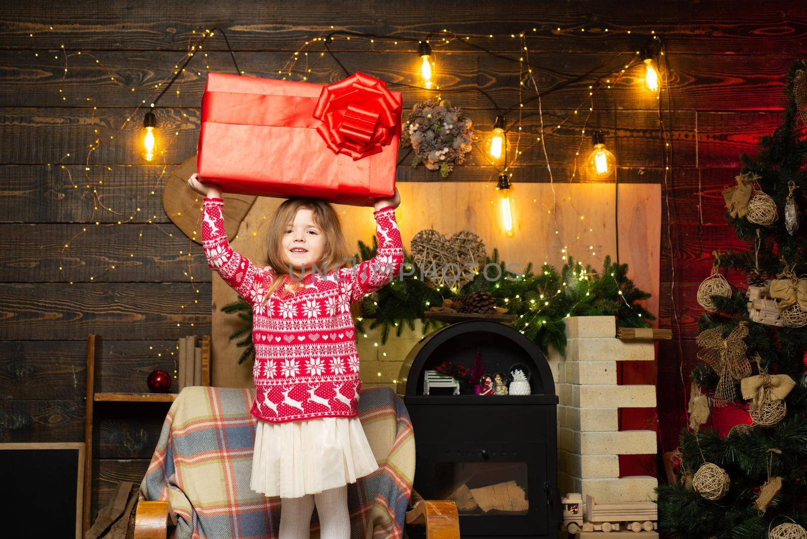 The concept of giving and receiving gifts. Cheerful smiling happy little cute girl holding gigantic gift present from Santa. Christmas eve and magic concept. Bright New Years interior