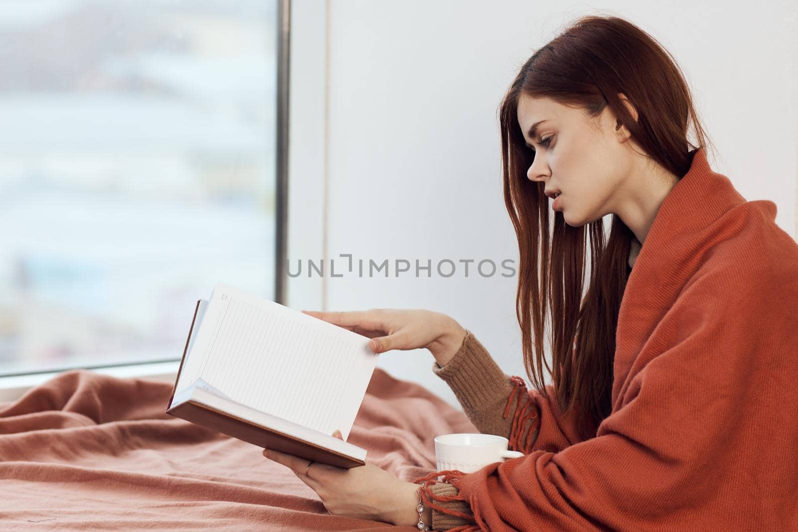 woman near the window with a plaid reading a book rest. High quality photo