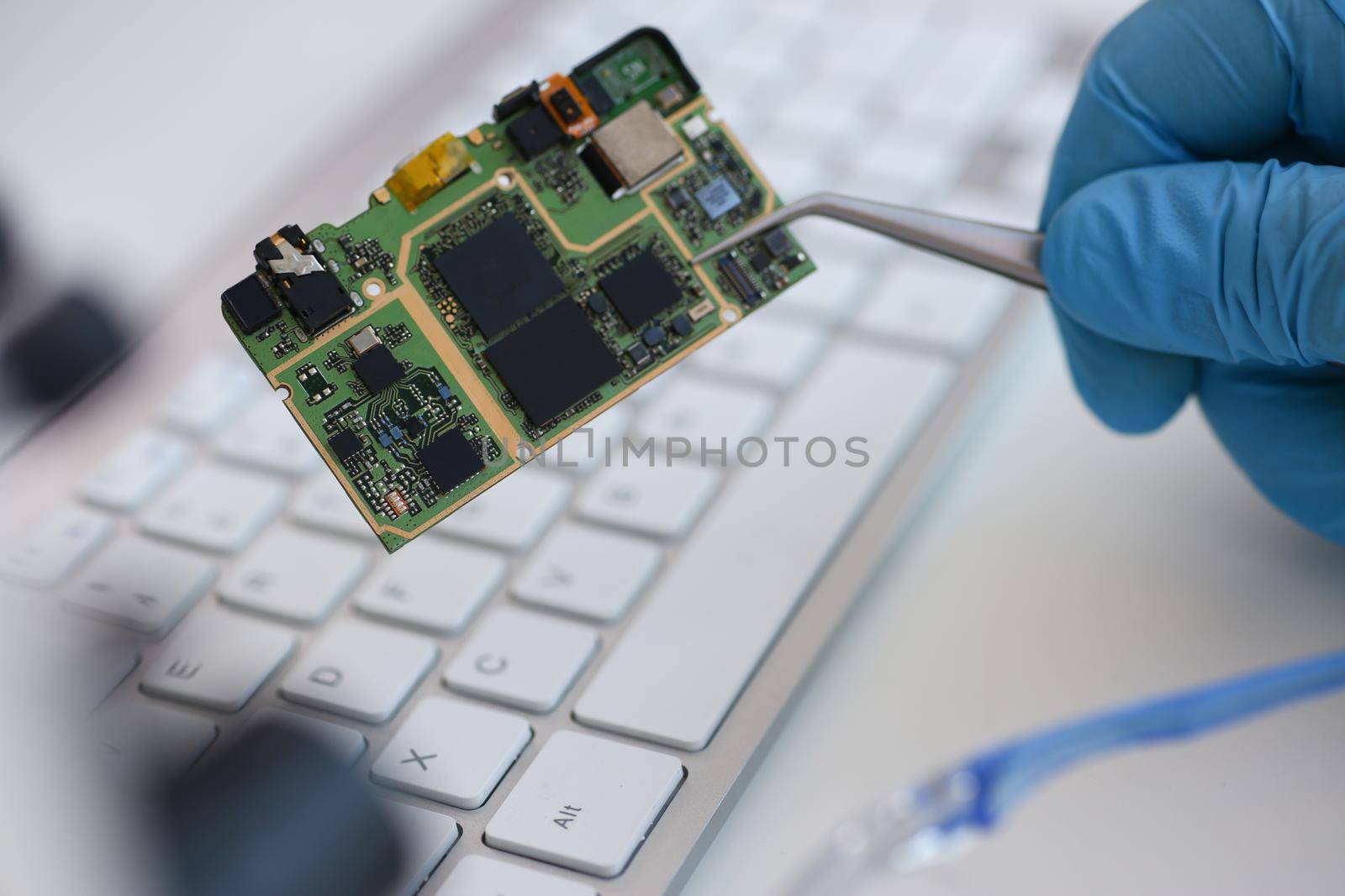 An employee of computer repair service assembly keeps spare part motherboard processor with tweezers for installation using method of soldering technology development