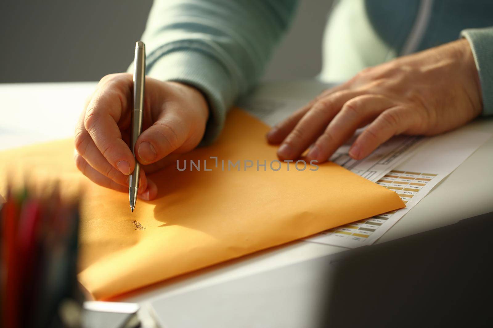 Male hand holding silver pen. Fill in address on yellow envelope of mail correspondence for application hiring concept