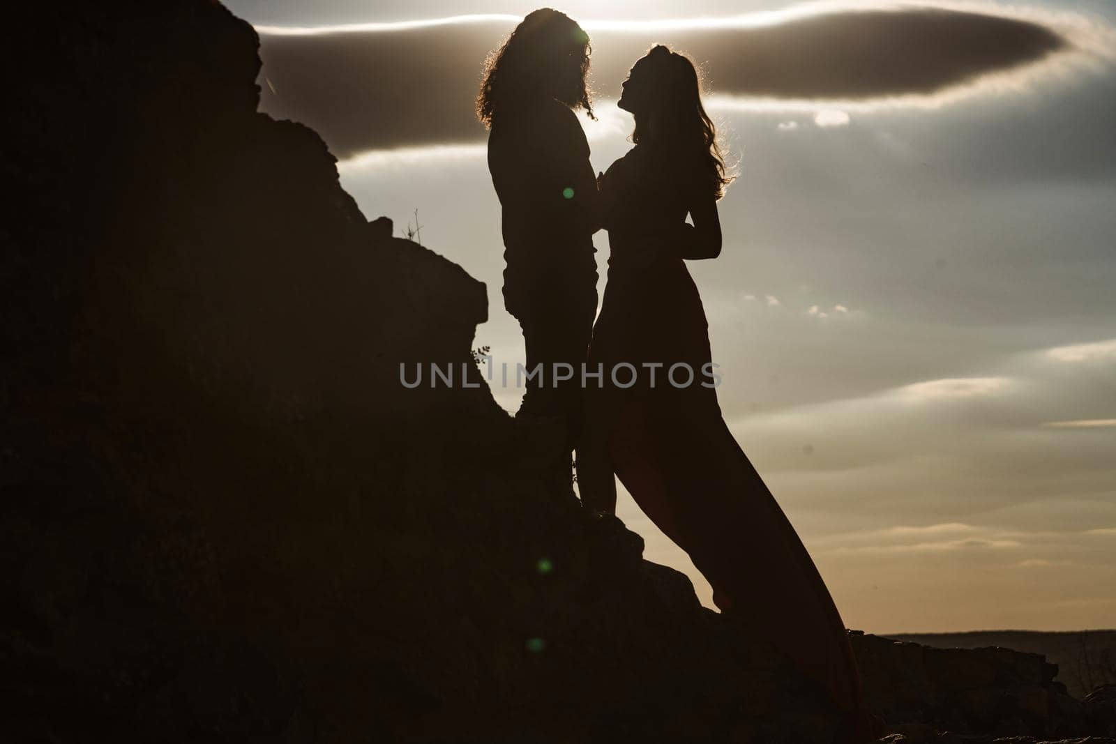 Silhouettes of love couple man and woman at rock mountain in beautiful nature sunset. Couple love concept. Shadow figures of man and woman holding hands. Love and relations. by Tverdokhlib