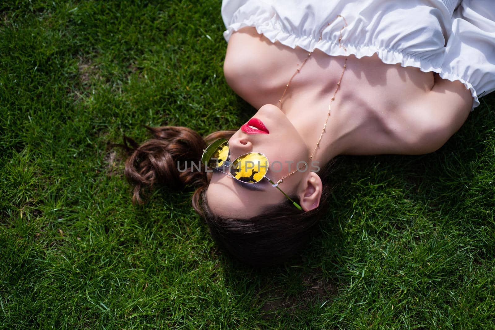 Girl in sunglasses enjoying nature lying on grass. Beauty trends. Copyspace. Summer reflection in sunglasses of beautiful young woman on grass. Summer vacation