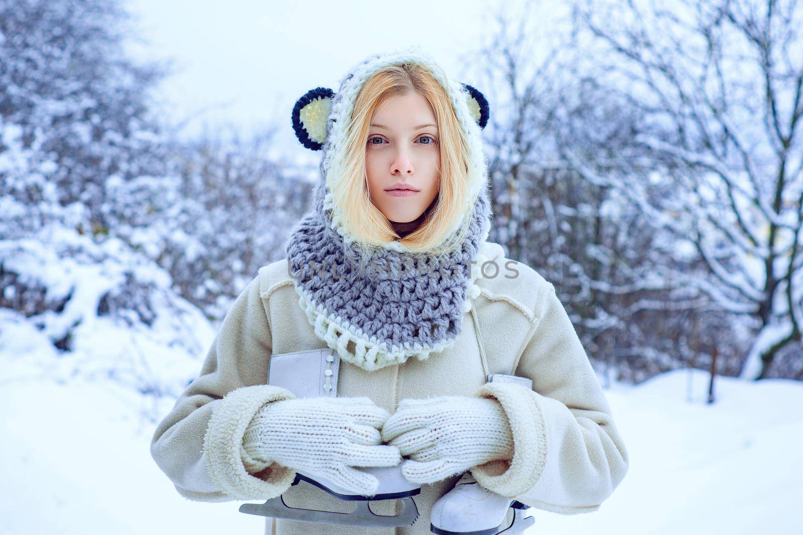 Winter woman. Young blond woman in sweater and funny hat holding white skates over shoulder in freezing winter day. Winter holiday. by Tverdokhlib