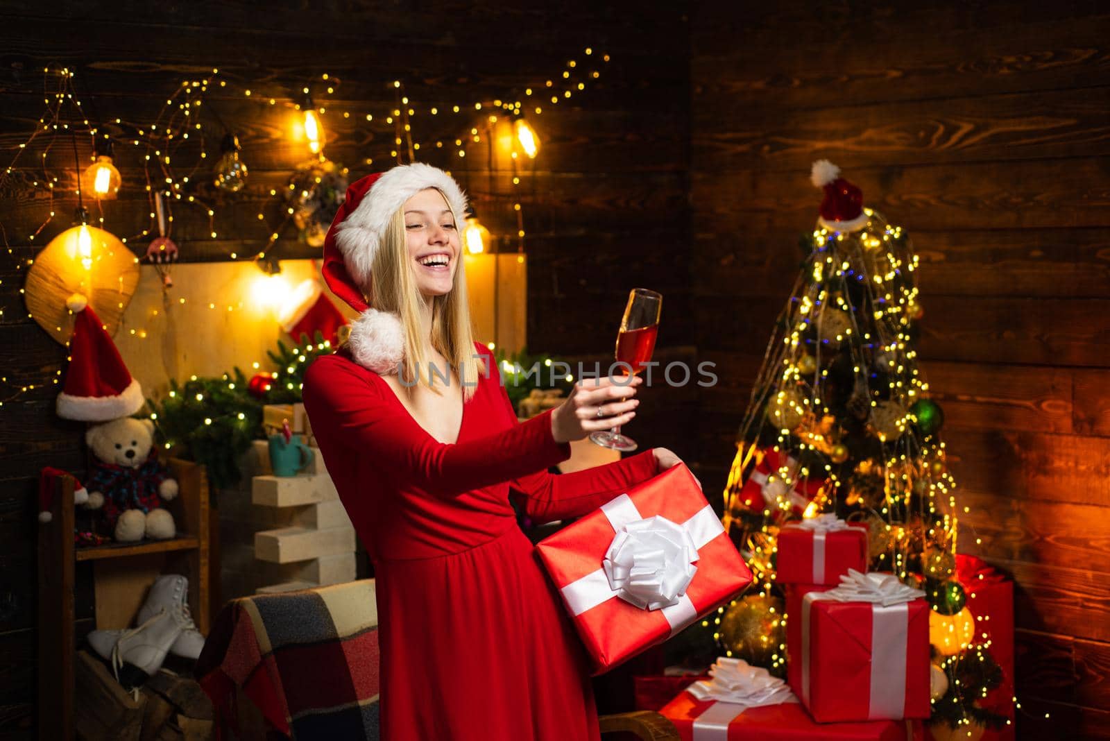 Young beautiful woman in Santa outfit holds Christmas present gift box at winter decorated background. Christmas eve. New Year surprise present. Indoor relaxation