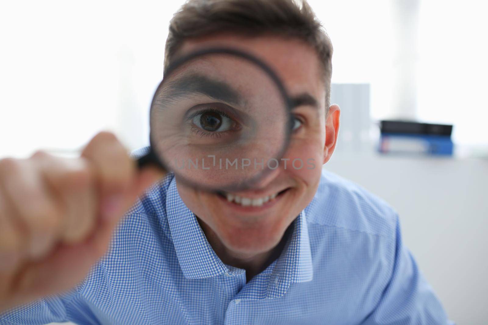 A businessman in blue shirt is holding a magnifying by kuprevich