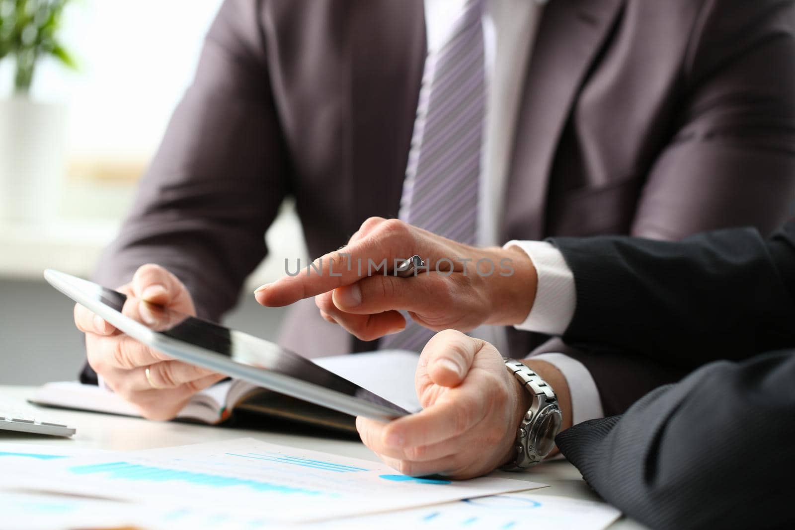 Two businessman are looking and studying statistics on tablet display closeup. Male hand opponent holds pen and points out problem collaboration business coach cooperation partnership palm concept