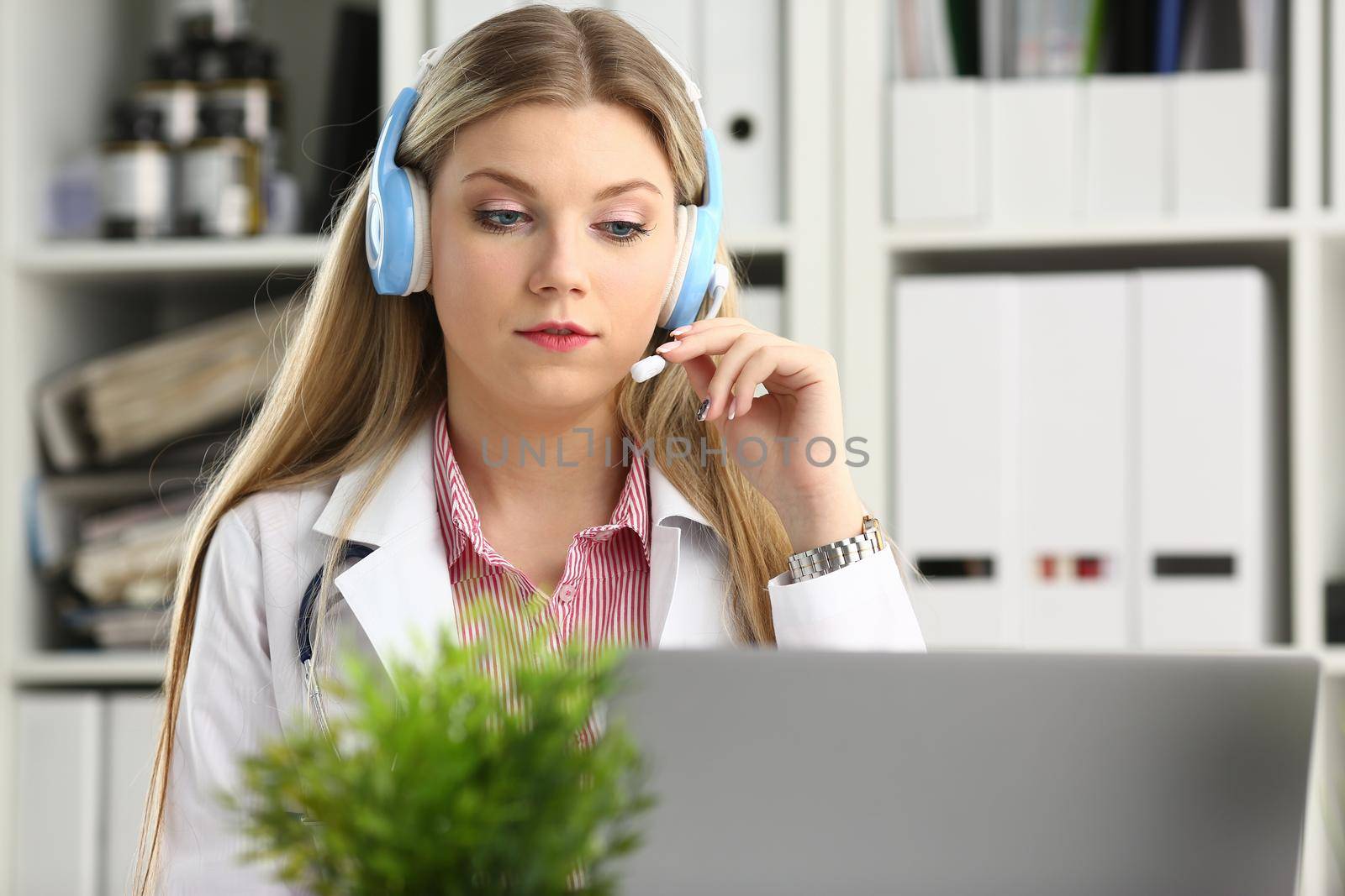 A beautiful feminine blonde doctor talking to patient over wireless headset advises a medical problem the formation of remote education internship callcenter specialist