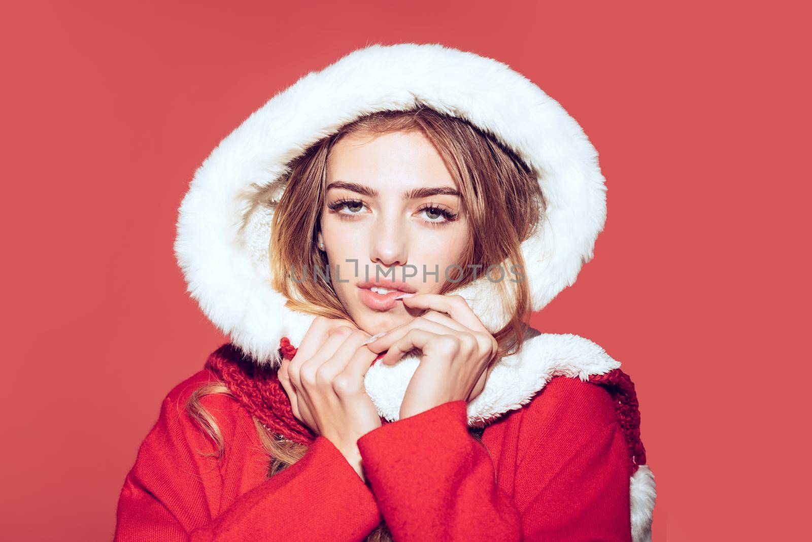 Woman in santa costume with pretty face. Xmas party and winter holiday. Happy girl celebrate new year on red background. Christmas woman in red hood, copy space.