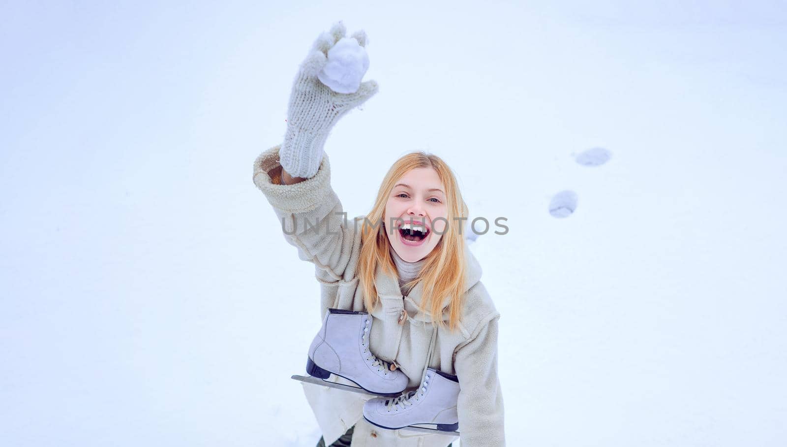Funny smiling young woman in wintertime outdoor. Happy winter fun woman. Winter game. Beautiful smiling young woman in warm clothing with ice skates