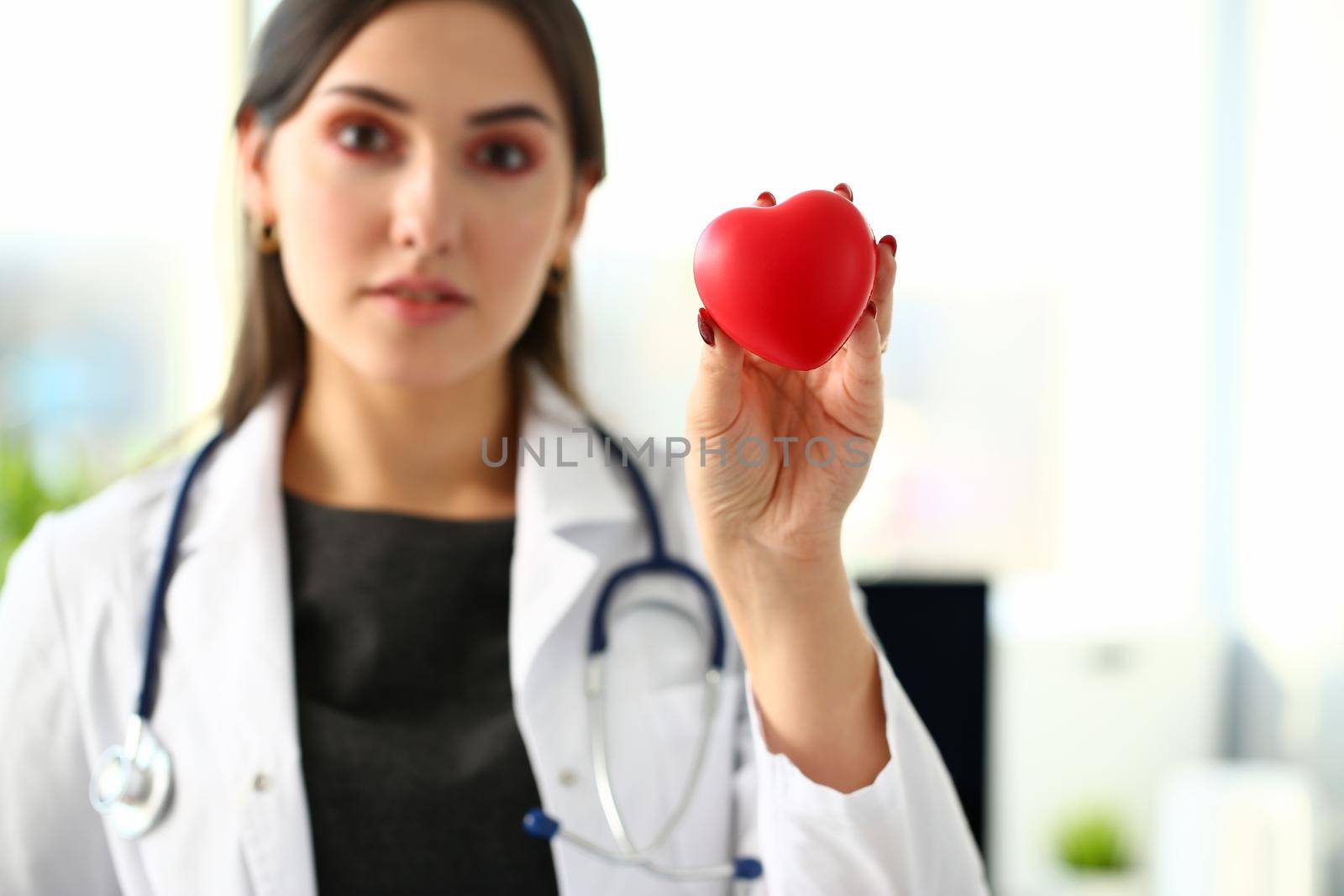 Beautiful smiling blond female doctor hold in arms red toy heart closeup. Cardio therapeutist student education CPR 911 life save physician make cardiac physical pulse rate measure arrhythmia