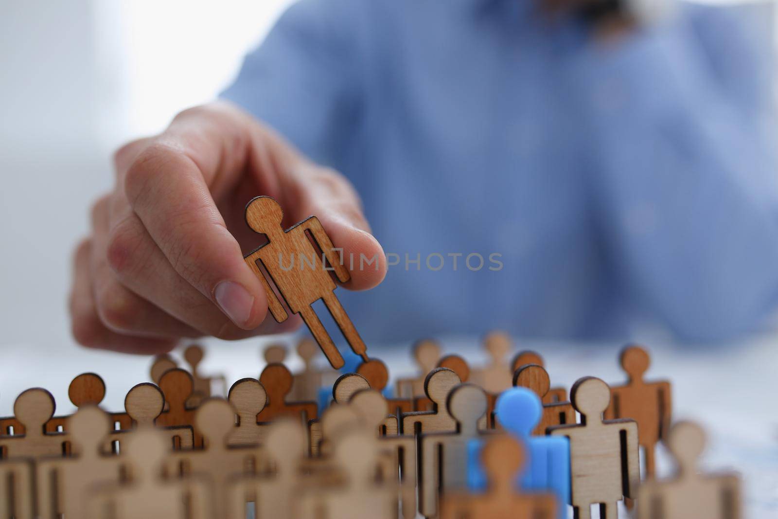 A businessman in blue shirt is holding object in his hand, is searching for personnel or people. Detective looking for missing person crowd of miniature figures choosing most suitable one