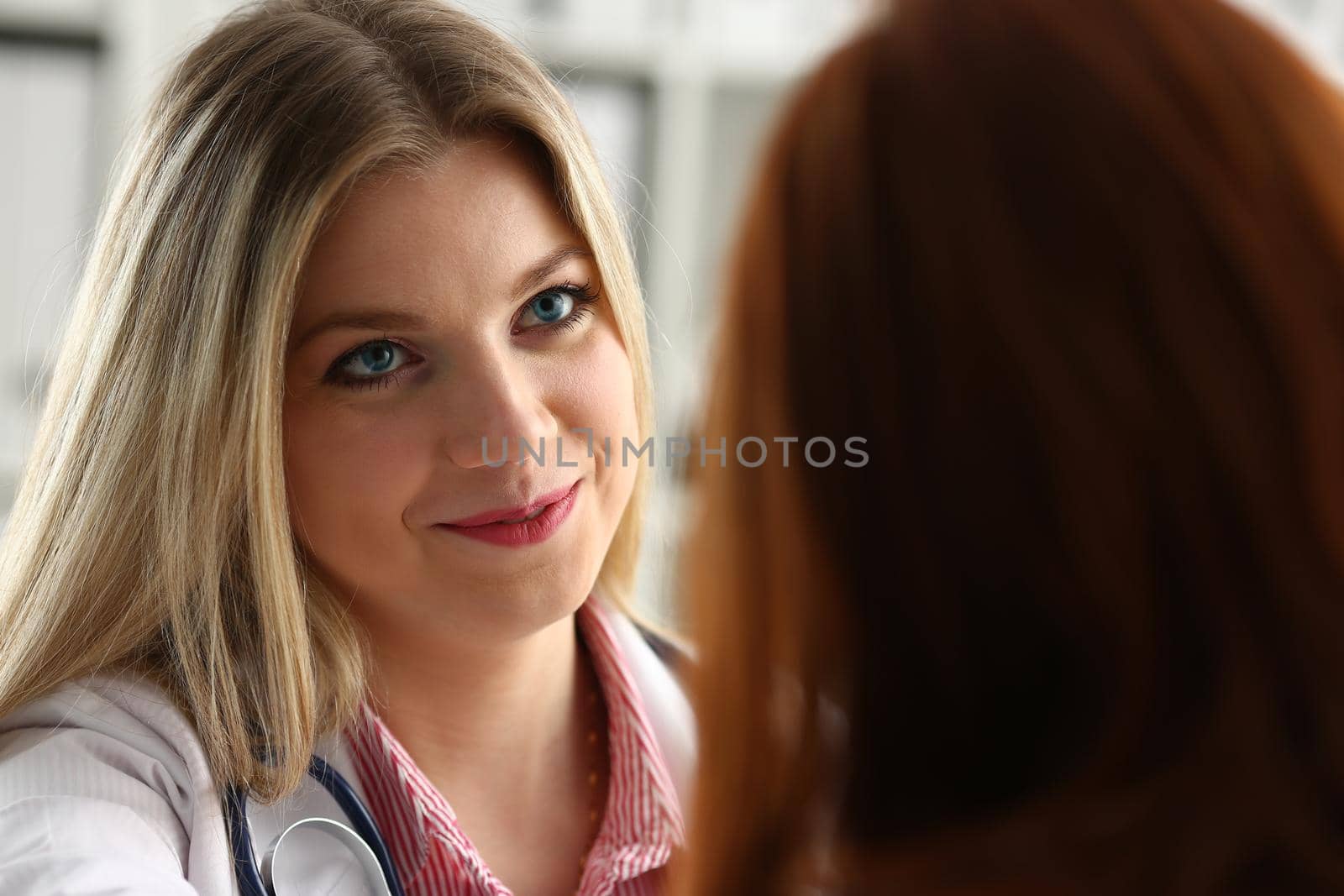 Handsome friendly female doctor talk with thankful female patient at office and greet her with hand on shoulder gesture. Welcoming friend trust physical healthy lifestyle exam interview concept