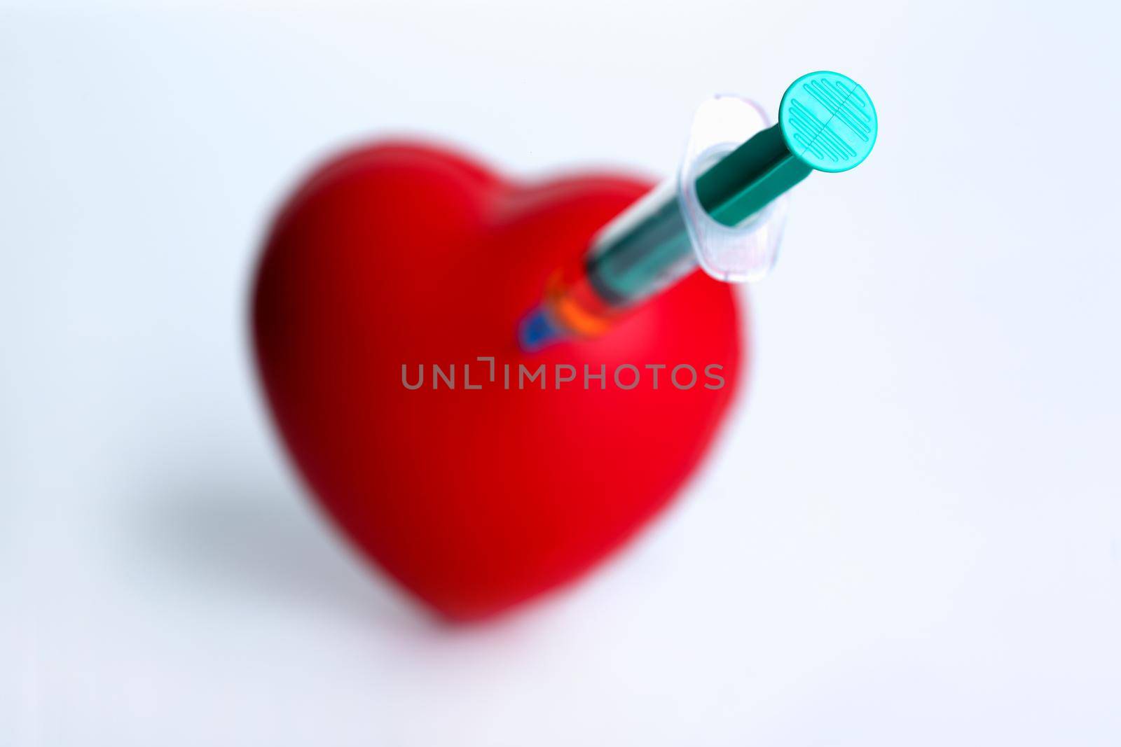 Red heart with stuck syringe on gray background. Cardiac surgery for introduction of an electric pacemaker concept