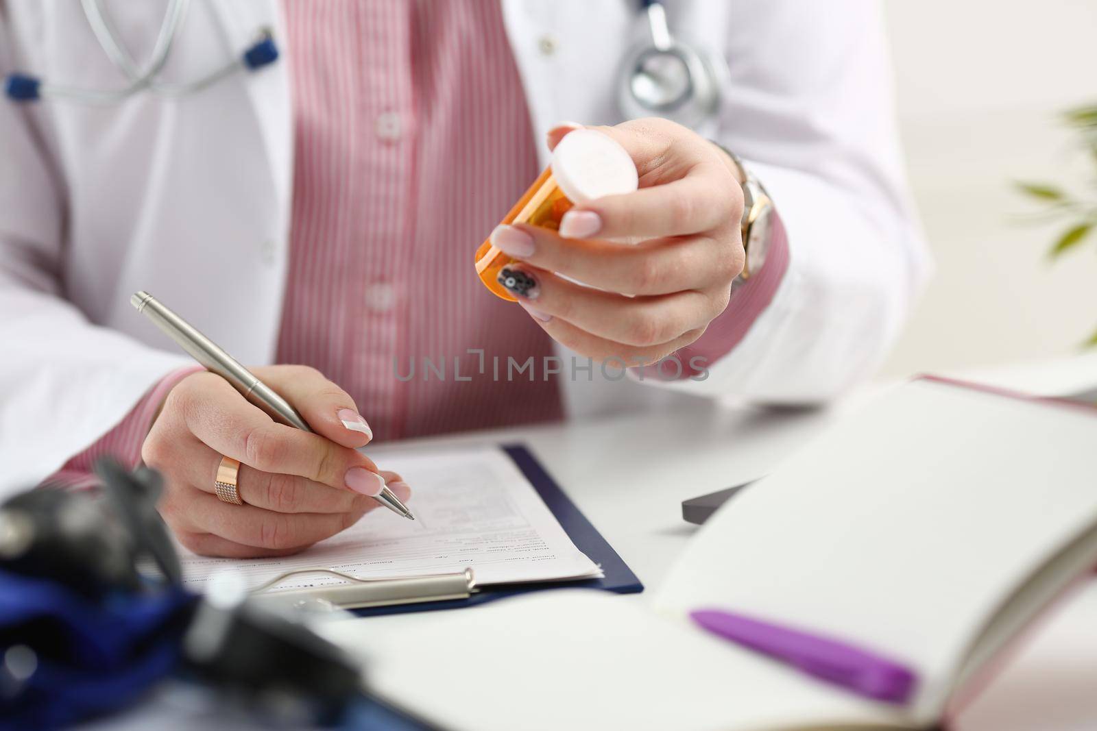 Female medicine doctor hand hold jar of pills and write prescription to patient at worktable. Panacea and life save, prescribing treatment, legal drug store concept. Empty form ready to be used