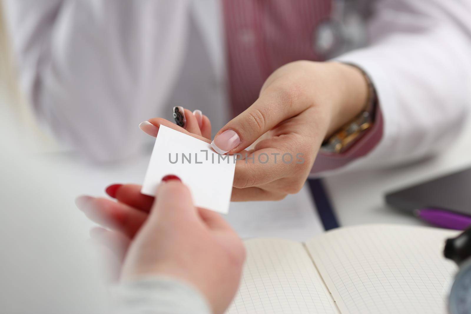 Female physician hand give white blank calling card to businesswoman closeup in office. Physical disease prevention examine patient instrument shop healthy lifestyle family doctor concept