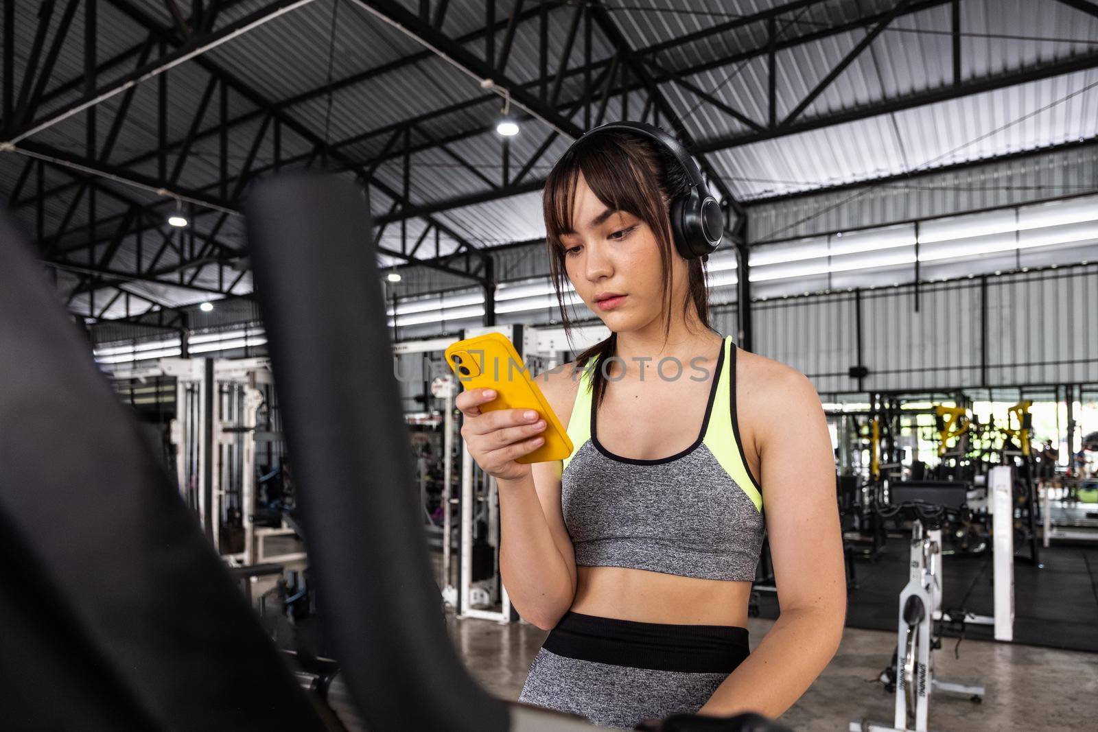 Young asian happy woman sitting and listening to music by smartphone while having exercise break at the gym.