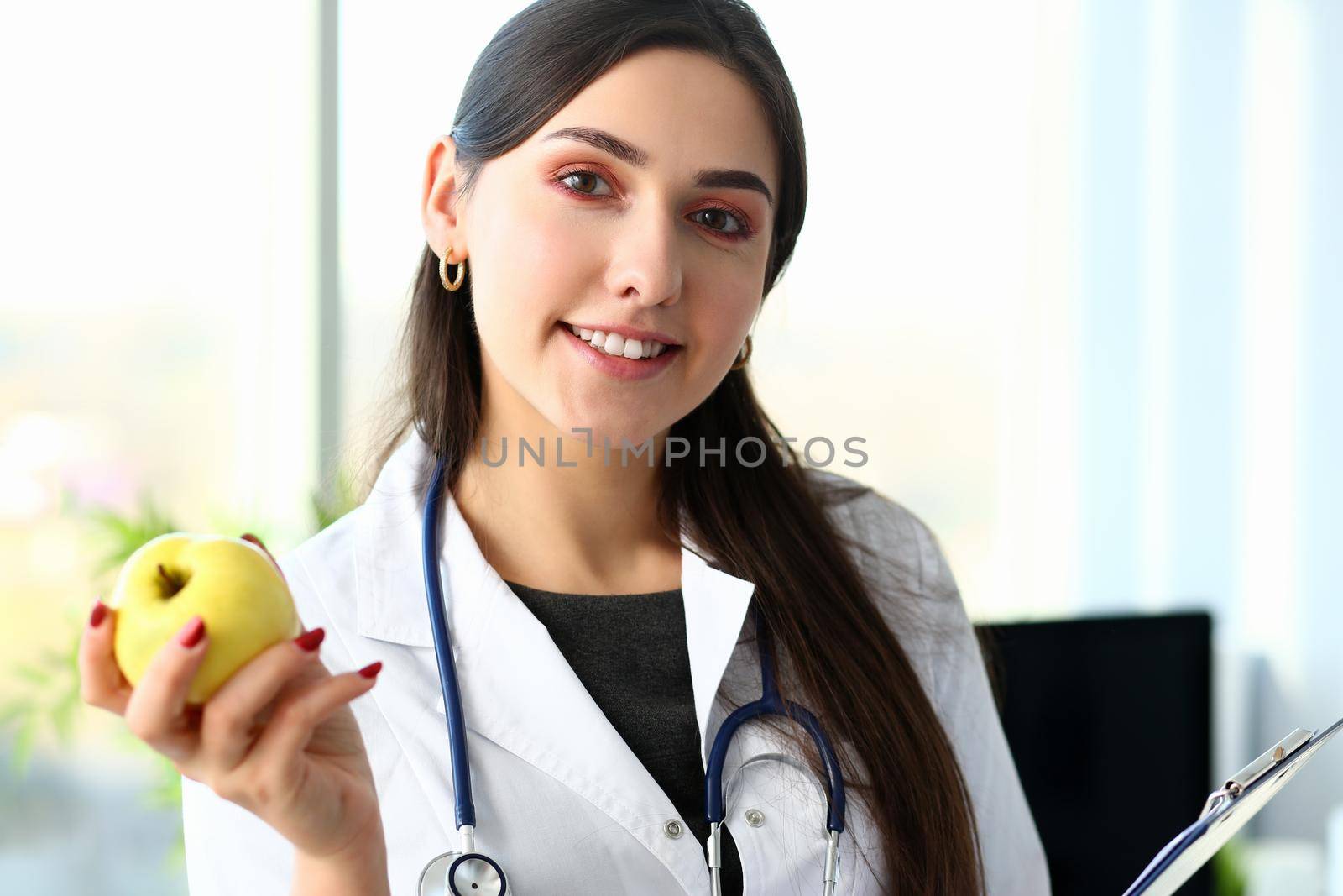 Young smiling woman doctor holds apple in hand portrait. Nutritionist talks about concept of healthy diet lifestyle for losing excess weight about benefits and harms vegetarianism.