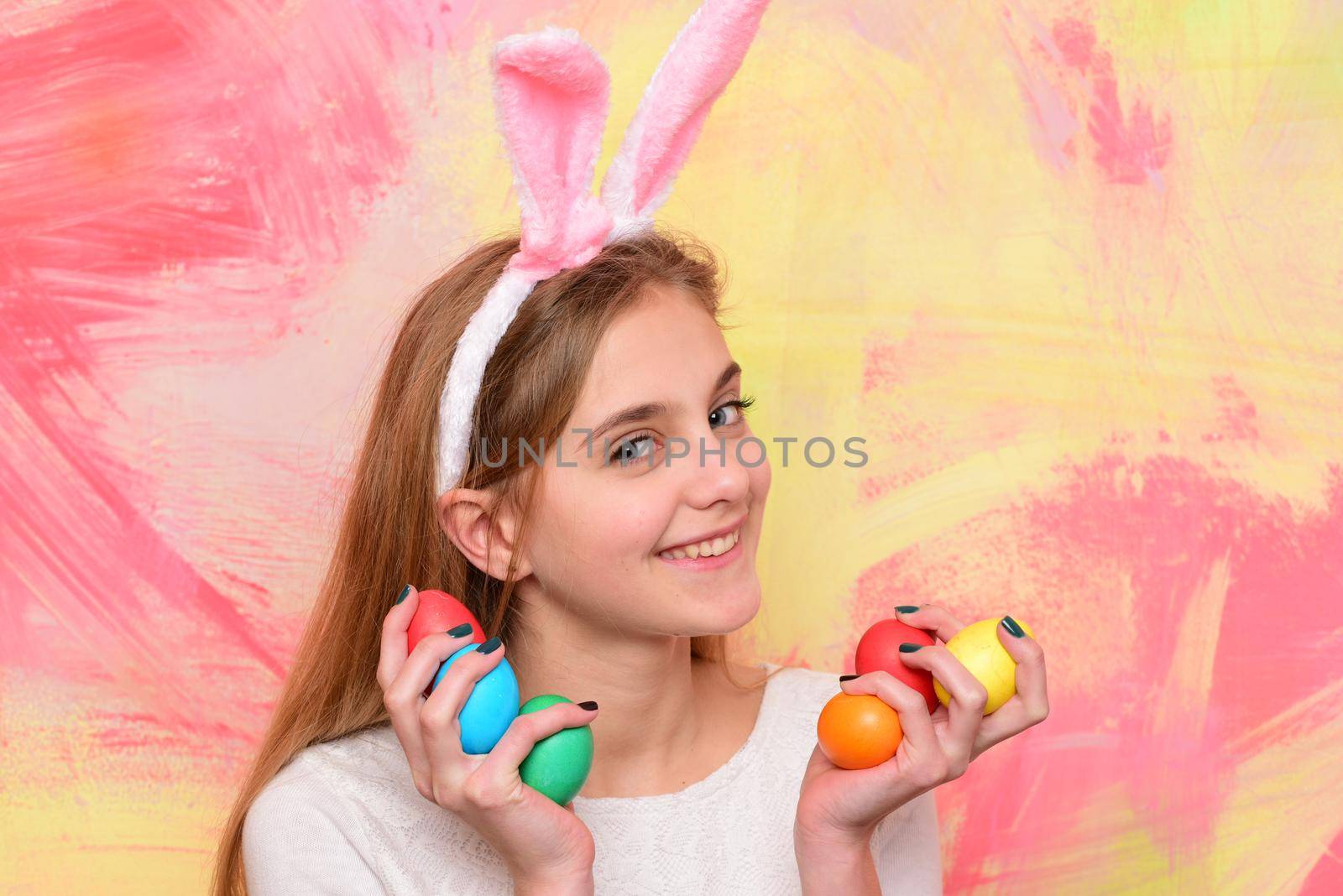 Happy smiling little teen girl with bunny ears holding painted easter eggs. Happy easter holidays concept. Cute girl celebrating easter. Cheerful kid with traditional decorations. by Tverdokhlib