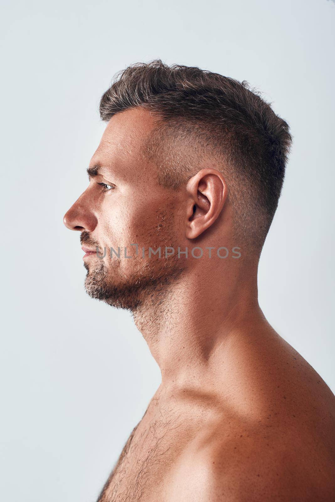 Studio shot of charming man with a stubble standing against grey background. Men beauty. Human face