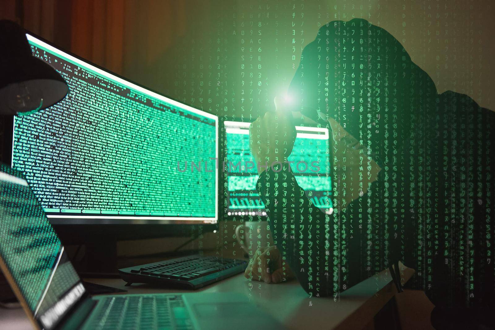 Cyber crime. Side view of young hacker in black hoodie using multiple computers and his smartphone for stealing data while sitting in dark room. Binary code. Cyber attack. Cyber security
