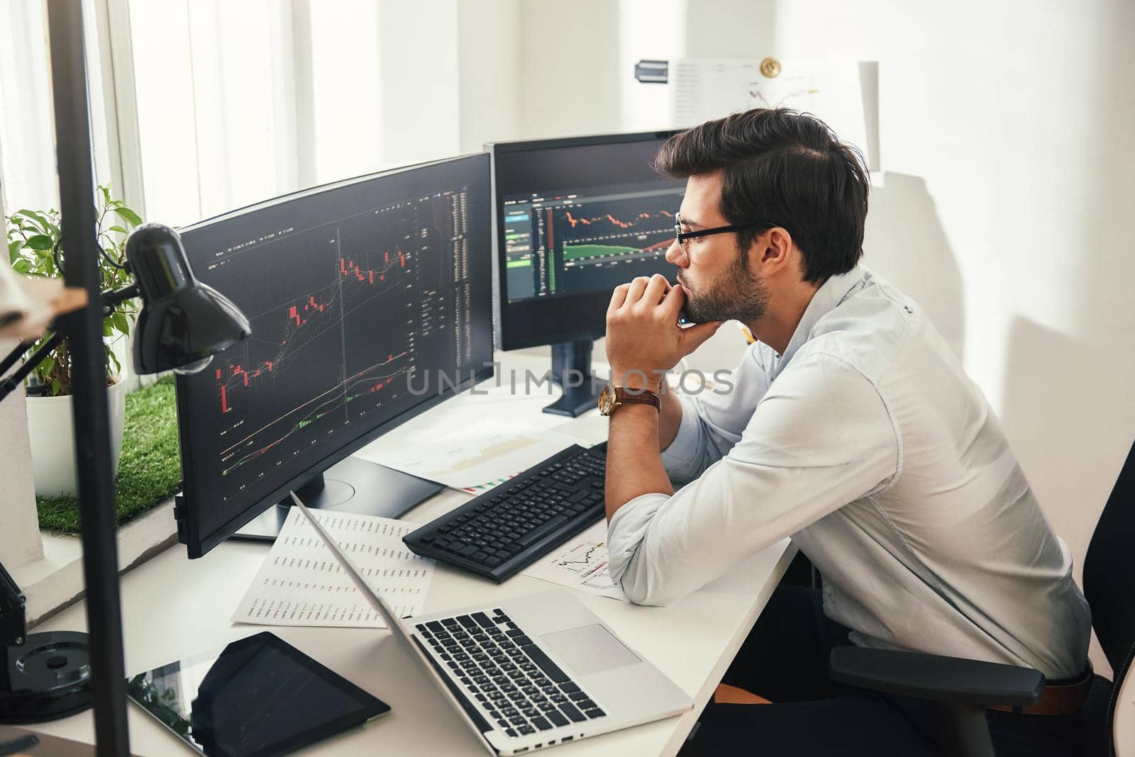 Successful trader. Back view of bearded stock market broker in eyeglasses analyzing data and graphs on multiple computer screens while sitting in modern office. Stock exchange. Trade concept. Investment concept