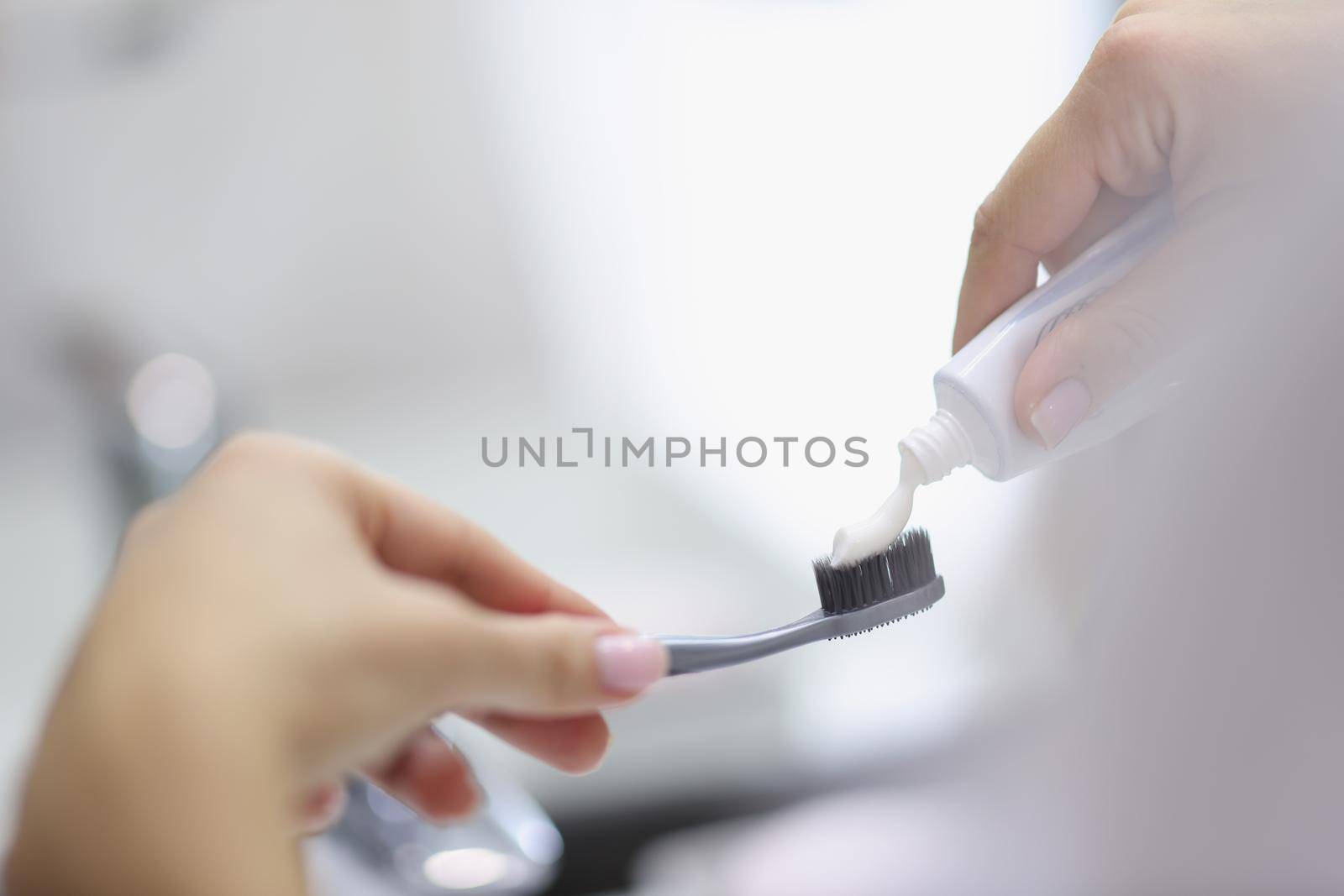 Female hands squeezing toothpaste onto brush in bathroom closeup. Daily oral hygiene concept