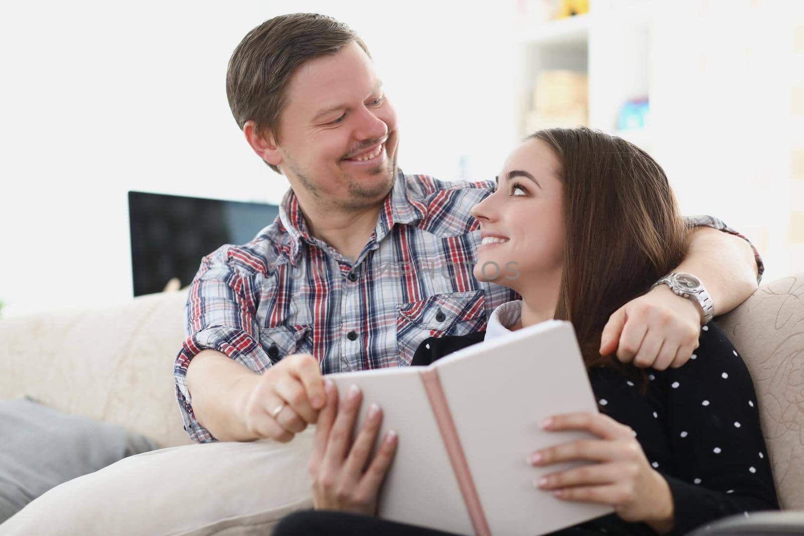 Young married couple sitting on sofa with book and looking at each other. Romantic relationships in family concept