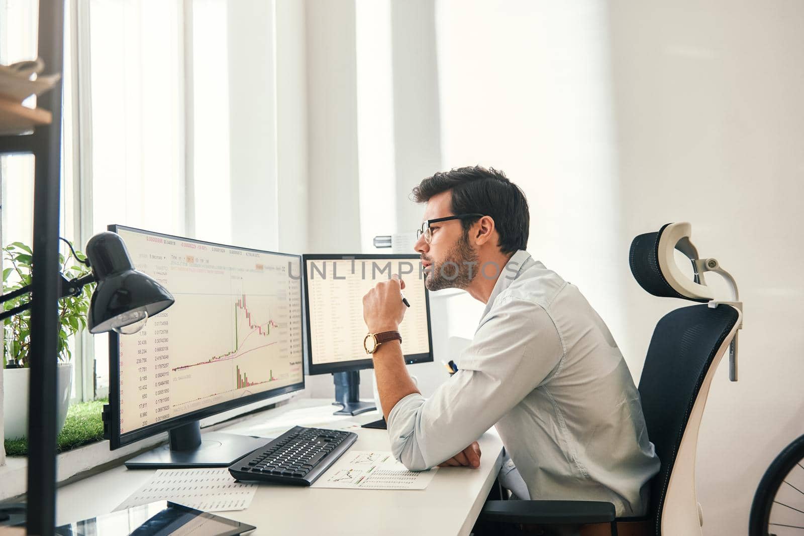 Busy working. Handsome bearded trader in formal wear and eyeglasses is analyzing trading charts and financial data on computer screens while sitting in his modern office. Stock exchange. Trade concept. Investment concept