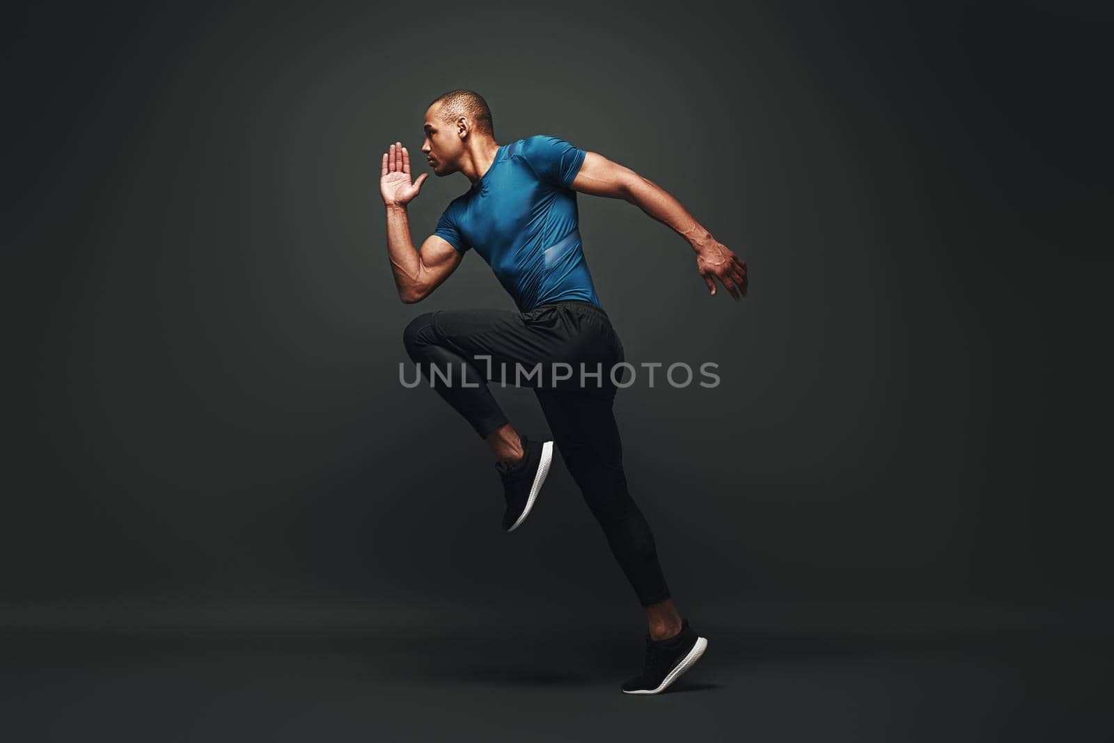 Full length portrait of a healthy muscular sportsman jumping isolated over dark background. Dynamic movement. Side view