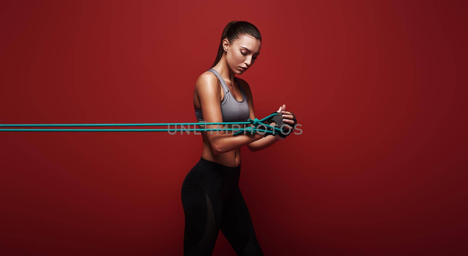 Sportswoman performs exercises for the muscles. Photo of young woman workout with resistance band isolated over red background. Strength and motivation.